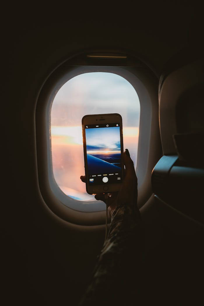 A person takes a photo of a sunset through an airplane window using a smartphone.