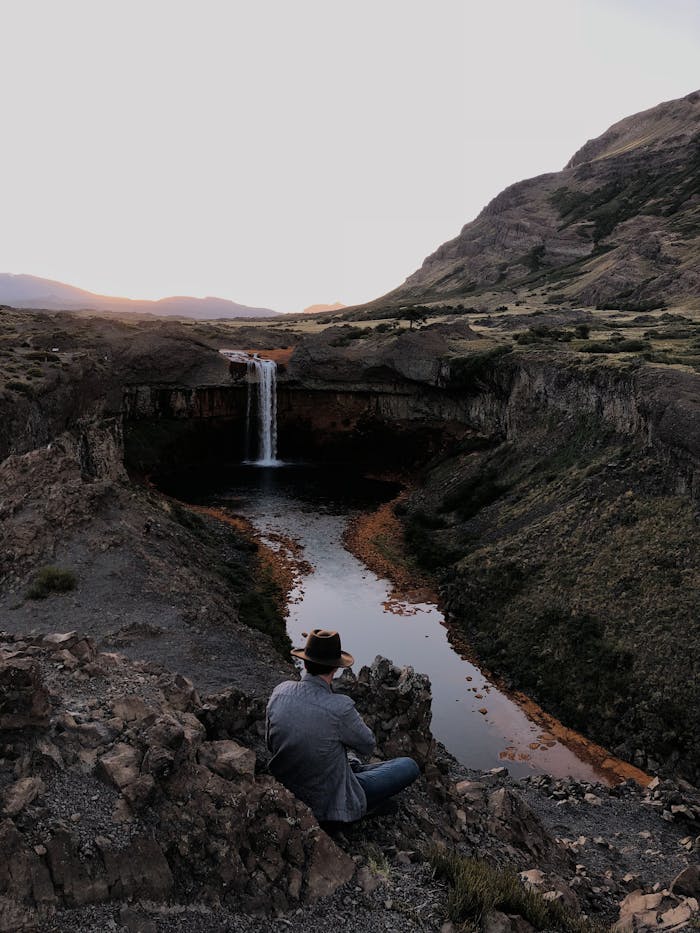 A lone traveler by a waterfall, surrounded by a dramatic landscape.