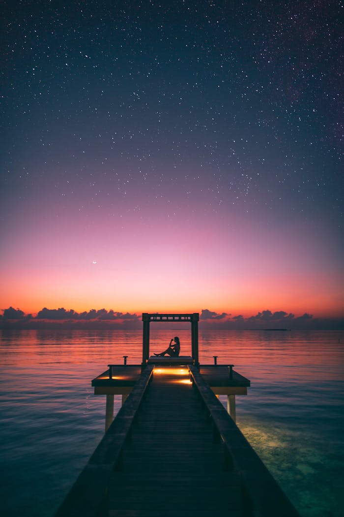 Tranquil scene of a person relaxing on a Maldives jetty at twilight under a starry sky.