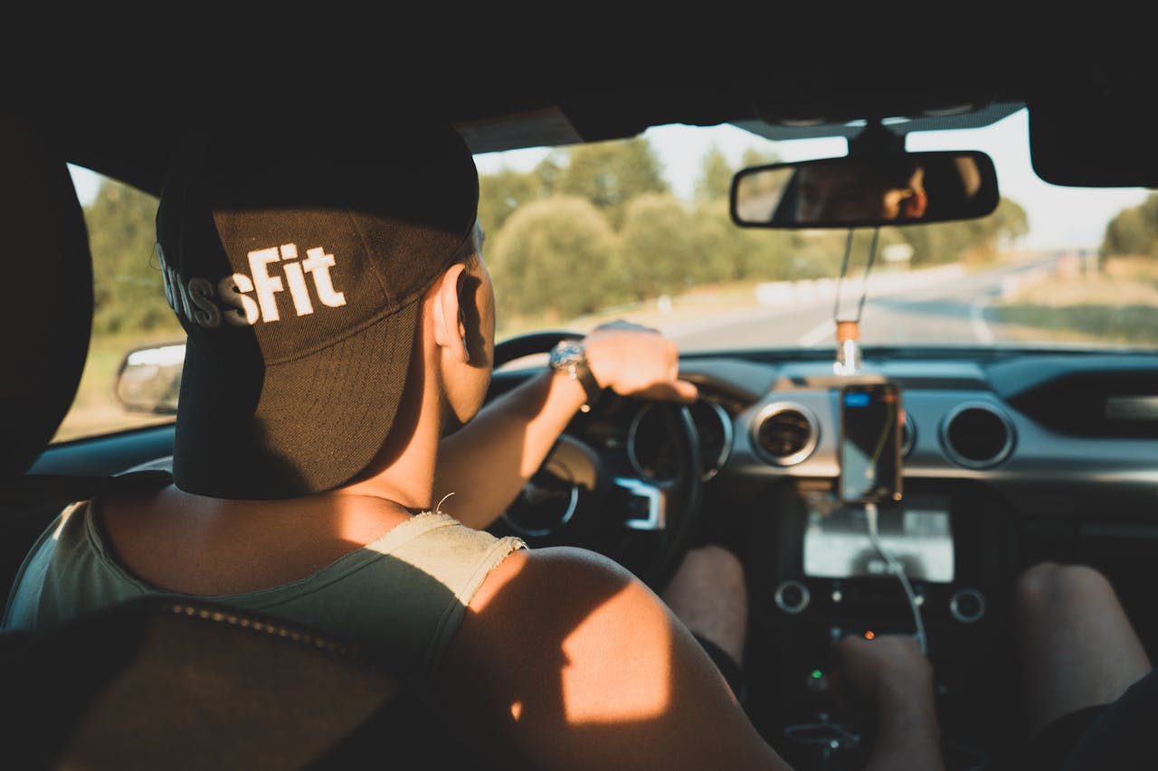 View of a young man driving a car on a rural road, shot from behind in warm lighting.